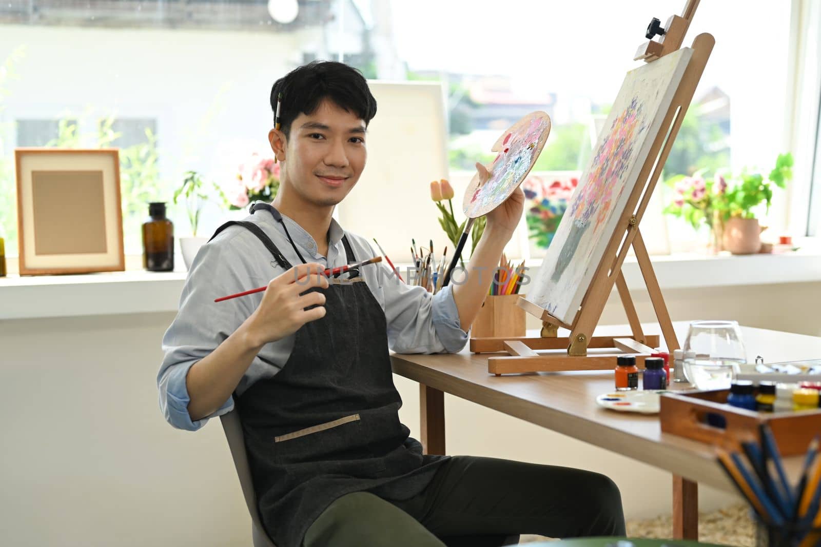 Image of pleased man artist painting picture with watercolor on canvas in art workshop. Art, creative hobby and leisure activity concept by prathanchorruangsak