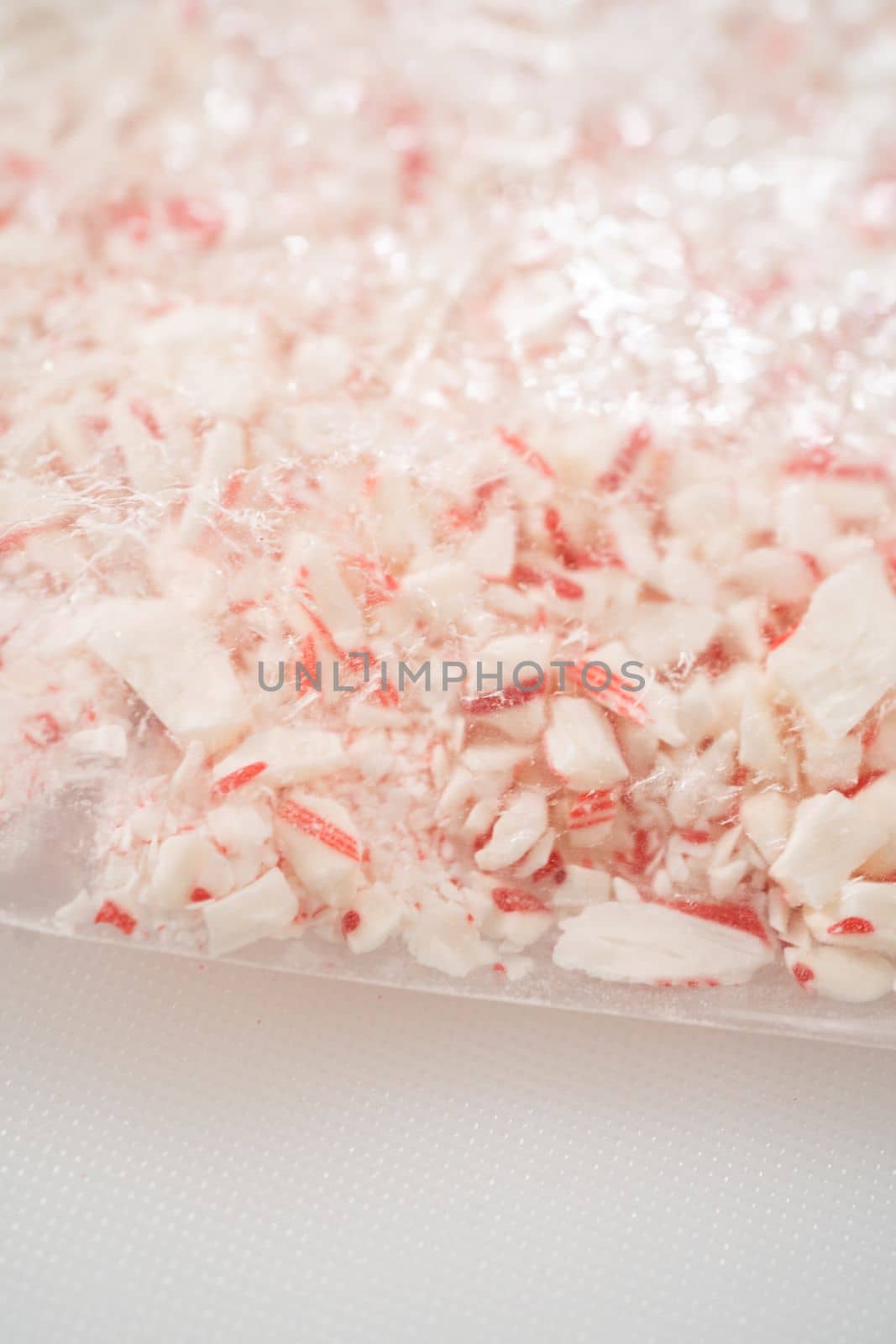 Crushing peppermint candies in a plastic bag with a marble rolling pin on a white cutting board.