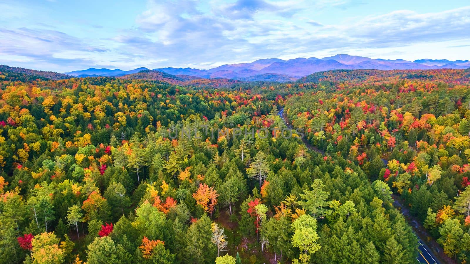 Image of Aerial over hills and mountains of peak fall forests with road winding through