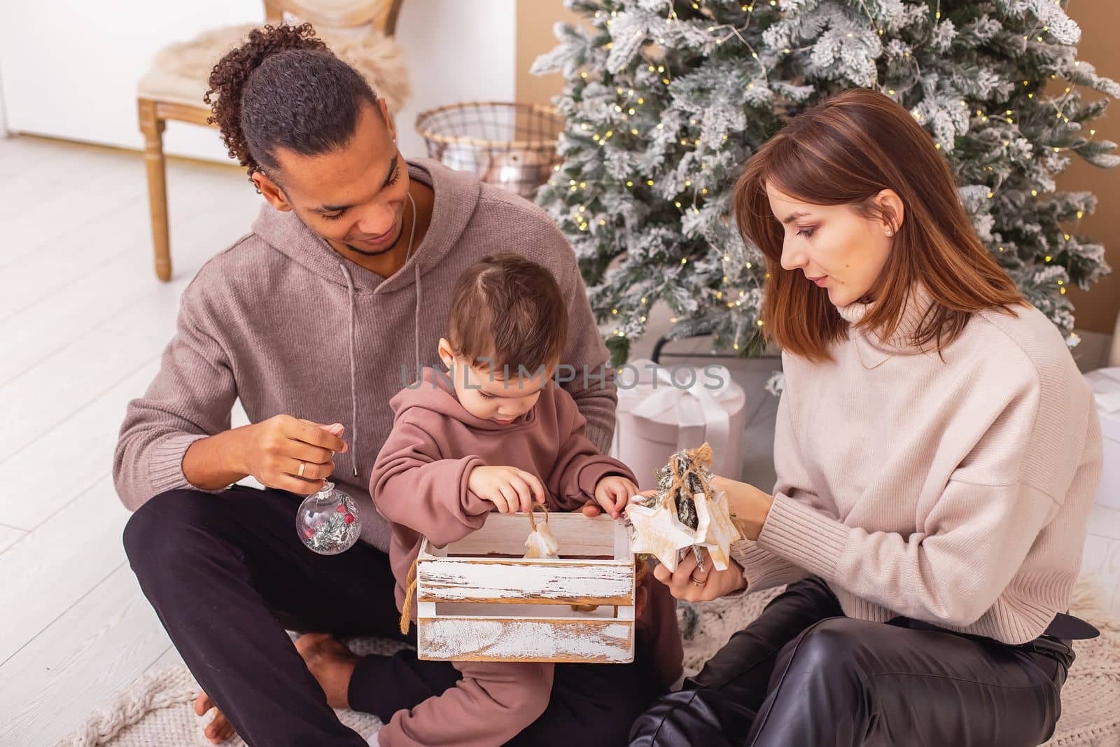 A multi-racial family is sitting holding a wooden box with Christmas toys. by Zakharova