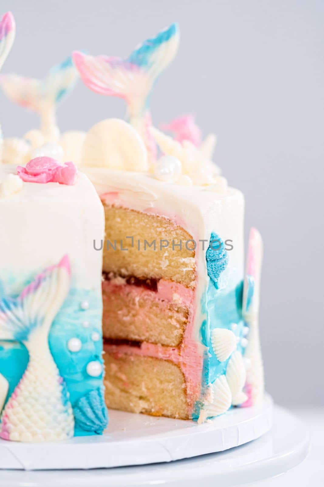 Slicing mermaid-themed 3 layer vanilla cake on a cake stand.