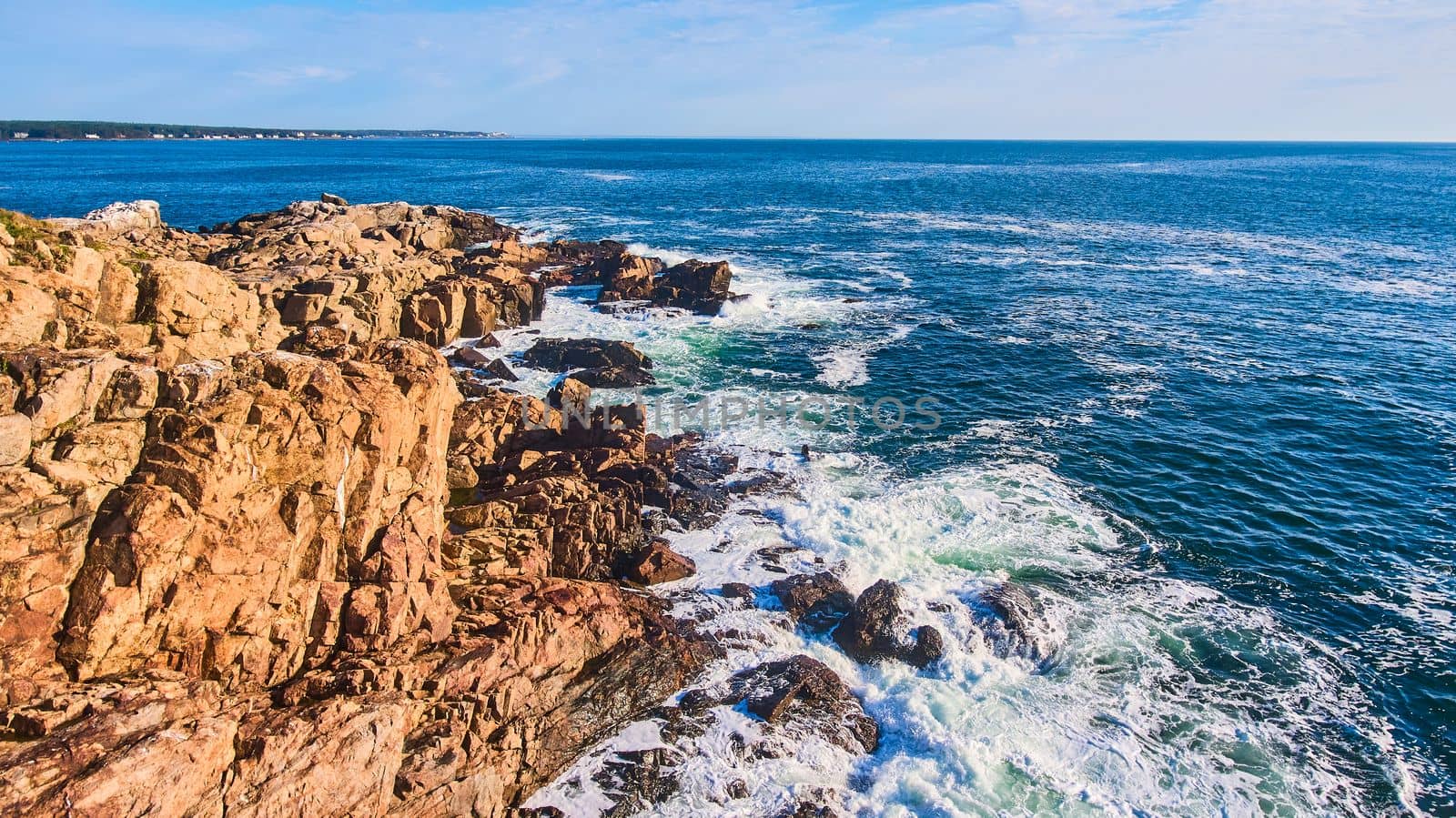 Cliffs of ocean in Maine with waves crashing over boulders by njproductions