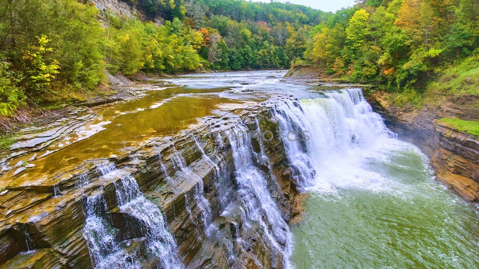 Image of Up close with drone to beautiful waterfall eroding cliffs with colorful forests around