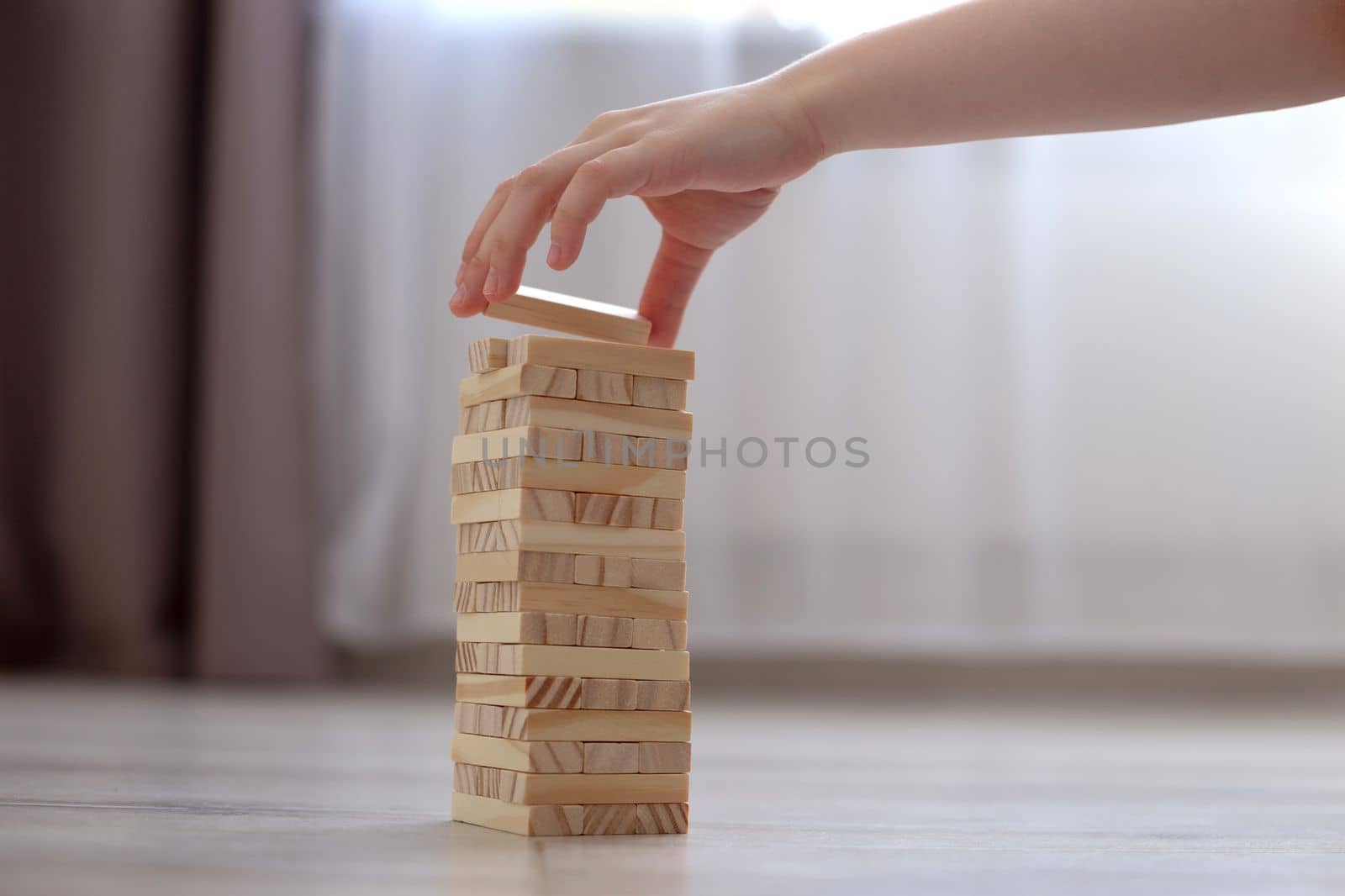 Childrens hand collects a tower of wooden blocks on the floor. Close up. Stay home in quarantine. Family board games