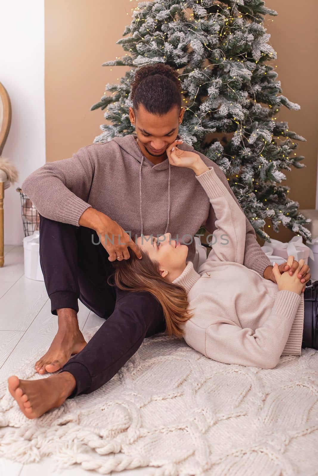 A young caucasian woman lies on the lap of a dark-skinned guy near the Christmas tree in the room, Vertical