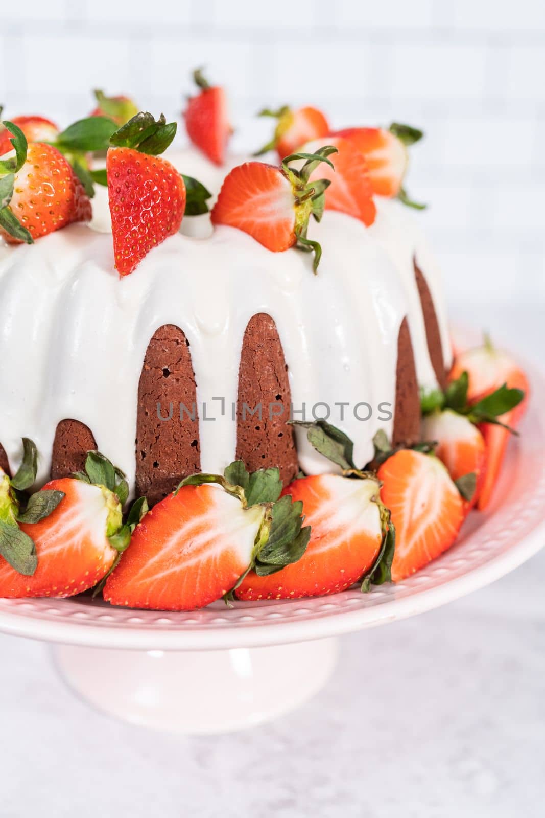 fresh strawberries..Red velvet bundt cake with cream cheese frosting garnished with fresh strawberries on a pink cake stand for Valentines Day.