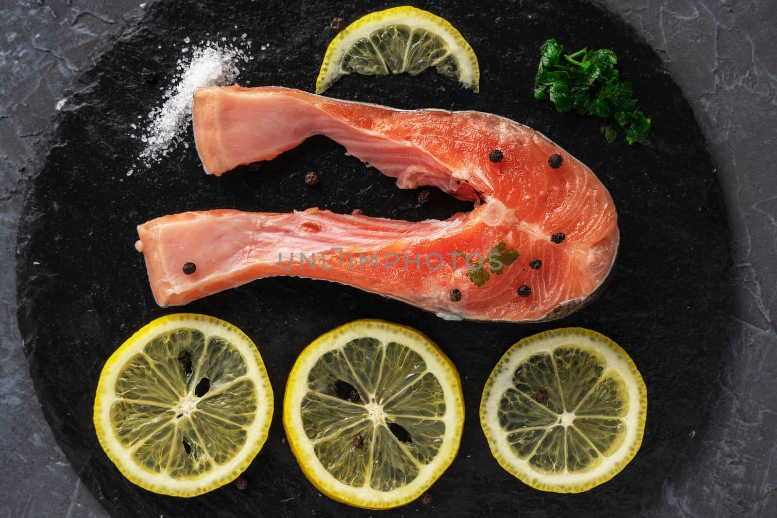 Fish steak with herbs, spices and lemon on a slate black board. Cooking fresh raw trout. Delicious juicy piece of trout for baking for dinner. High quality photo