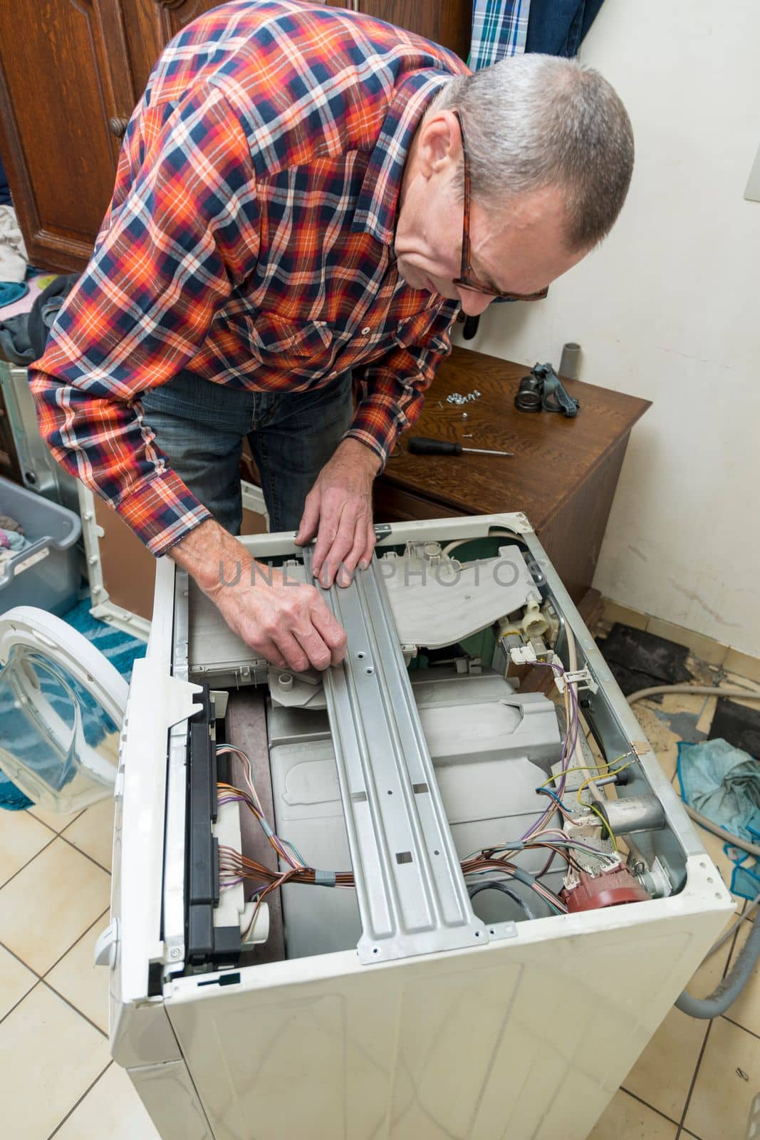 Middle aged man repairing broken washing machine with tools, household chores. High quality photo