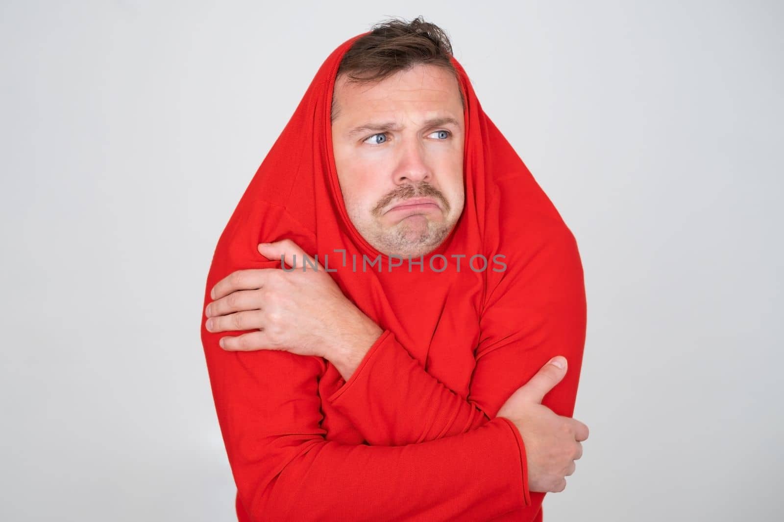 Young caucasian man ihiding pulling sweater on head in displeasure, keeps arms folded. 