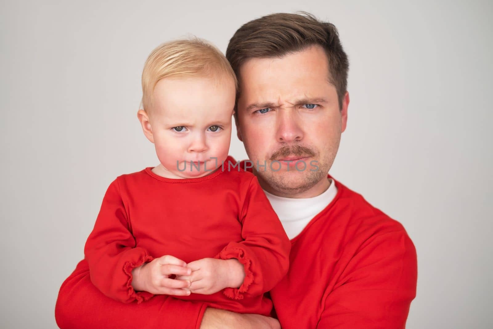 Caucasian father holding his baby daughter looking serious at camera at camera. Studio shot