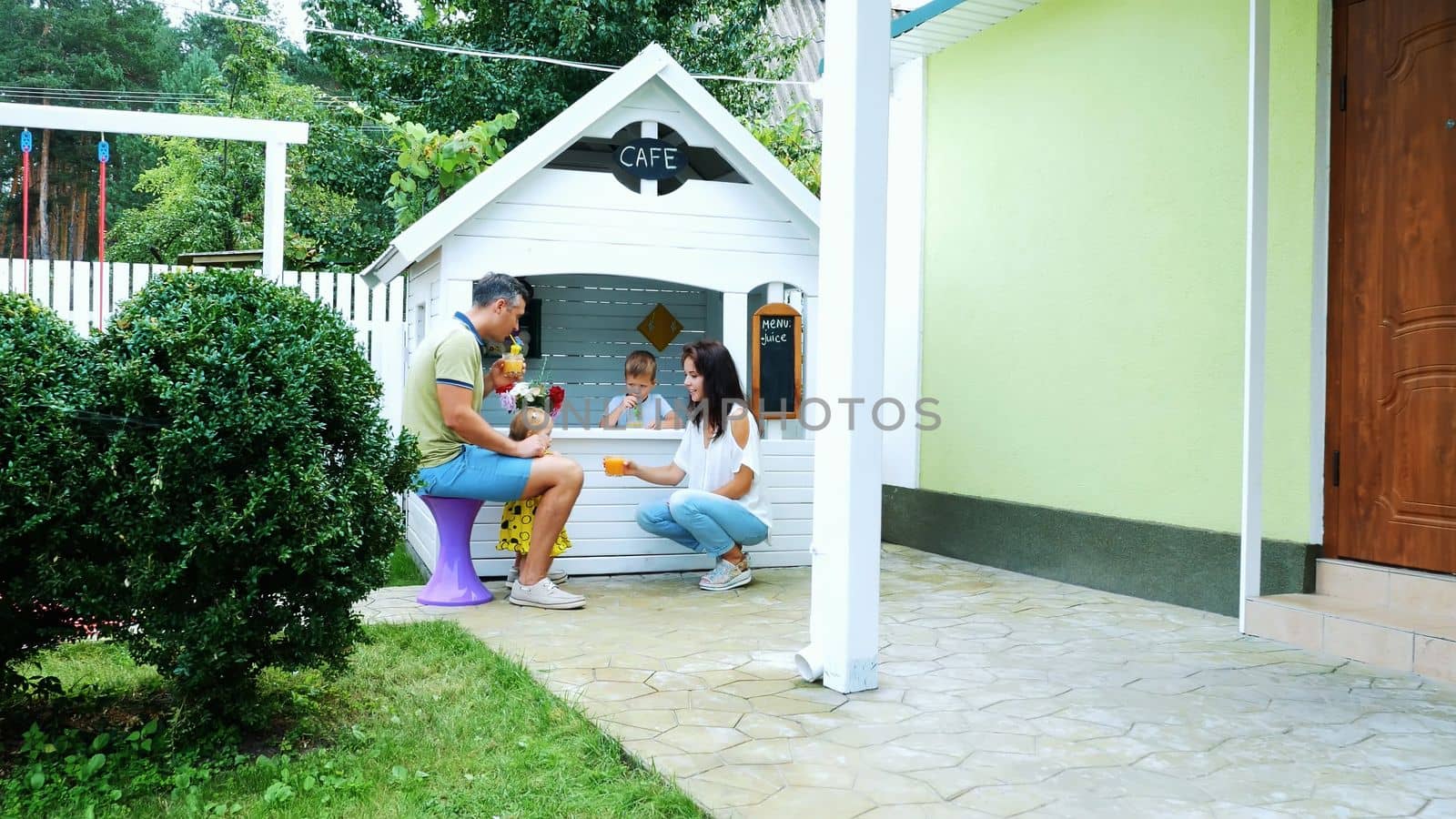 summer, in the garden, parents play with young children, a girl and a boy, in a cafe, in a children's play house, treat children with freshly squeezed fruit juices, drink juices. by djtreneryay