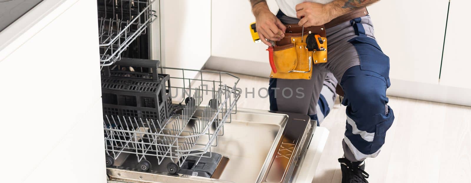 Closeup repair and installation of dishwasher, male worker with tool in uniform