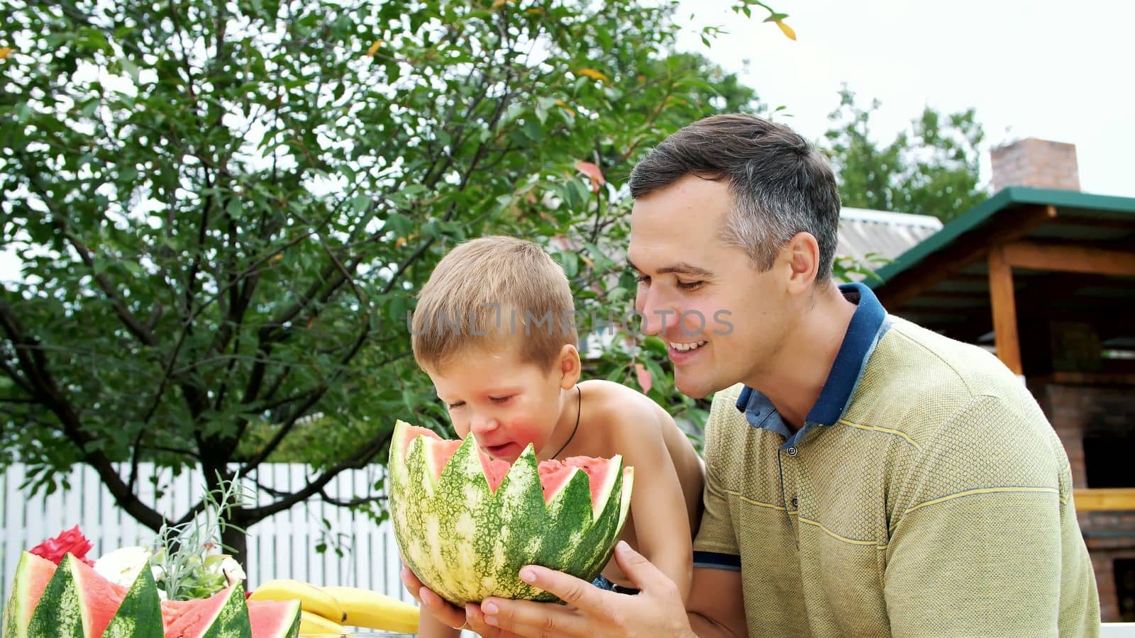 in summer, in the garden, father with a four-year-old son cut a watermelon and eat it, have fun, a boy likes watermelon very much. sweet watermelon for lunch with family. High quality photo