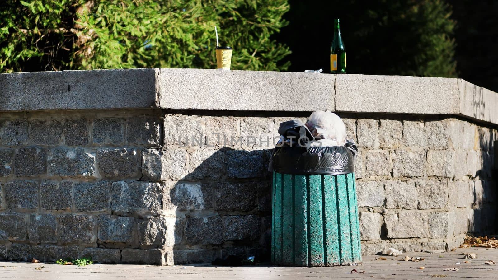 on street, sidewalk, is rubbish bin , filled to the top with trash, garbage. next to it are used plastic coffee cups, glass bottle of alcohol. ecology, pollution of the environment. High quality photo