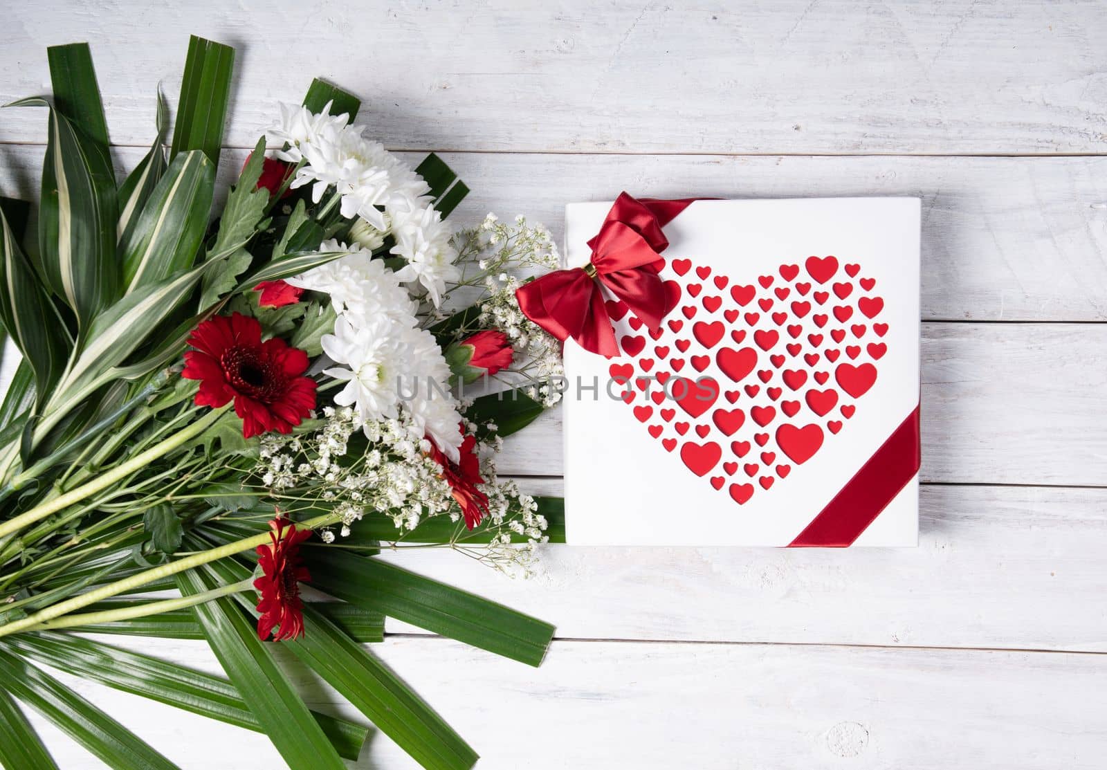 Valentine's day gift, red heart praline box and flower bouquet on white wooden table. High quality photo