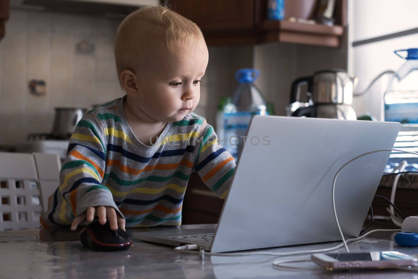 Little caucasian baby curiously looking at laptop surfing in internet, child and computer concept. 
