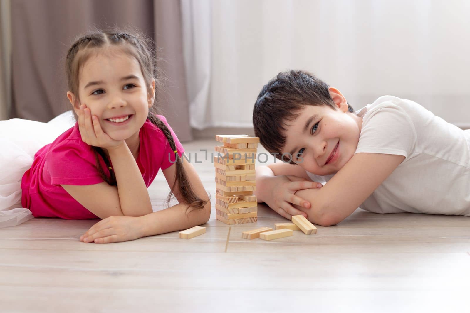 Smiling two children playing wooden game lying on the floor.Selectiv focus