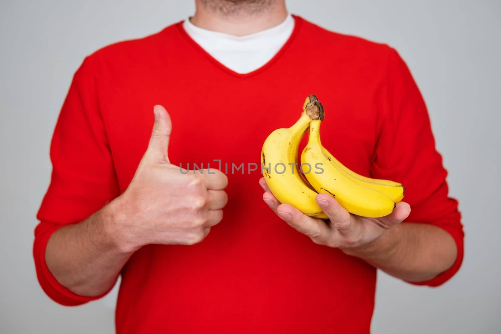 Caucasian man holding banana showing thumb up doing excellent and approval sign 