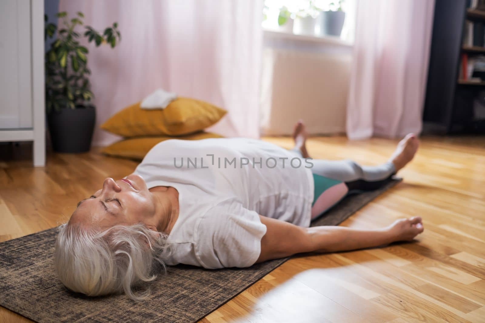 Senior caucasian woman lying on yoga mat after workout. Fit female relaxing on floor at home. 