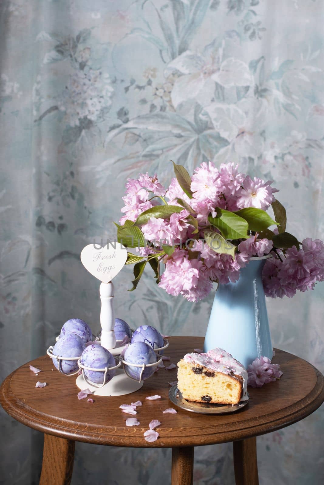 Easter cake and painted eggs and a bouquet of pink sakura flowers on a table by KaterinaDalemans