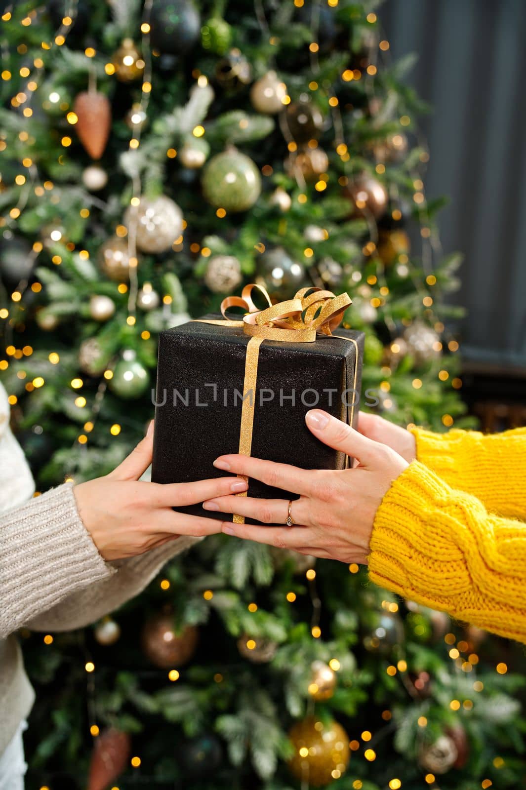 Gift Exchange in Front of Decorated Christmas Tree. Closeup of adult hands holding Christmas present in wrapping paper. by PhotoTime