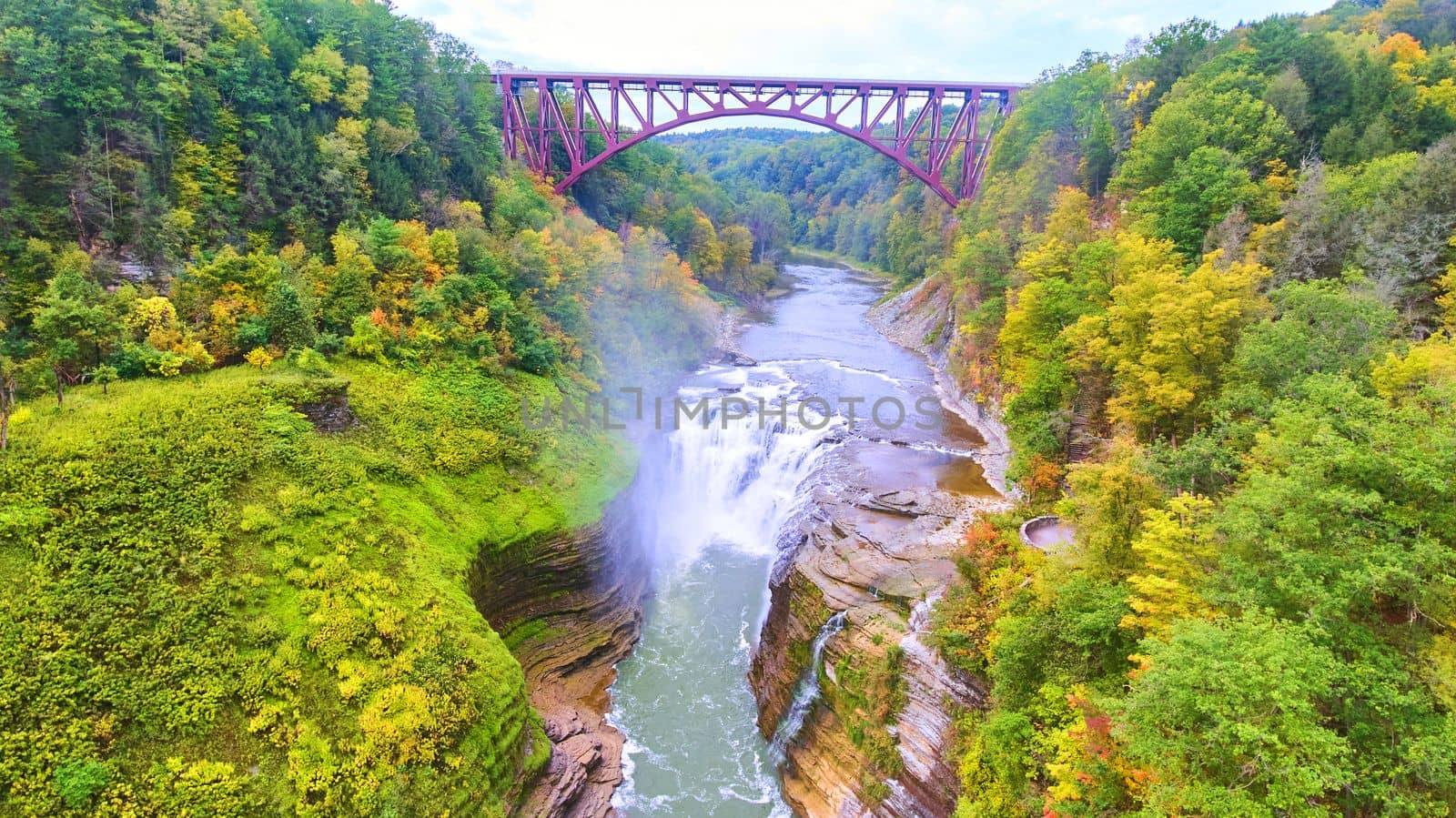 Image of Drone over amazing raging waterfall carving into cliffs with train track bridge above