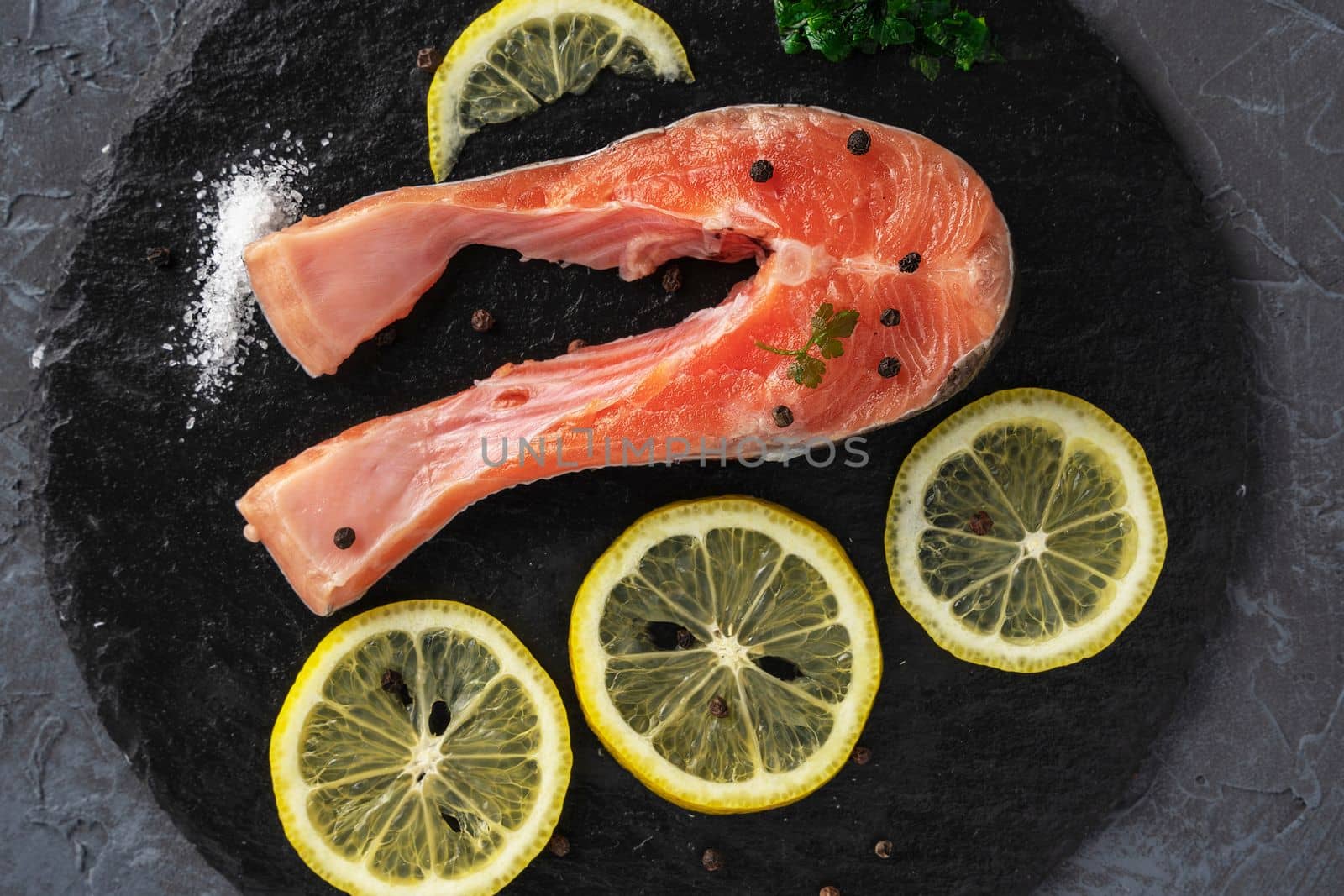 Fish steak with herbs, spices and lemon on a slate black board. Cooking fresh raw trout. Delicious juicy piece of trout for baking for dinner. High quality photo