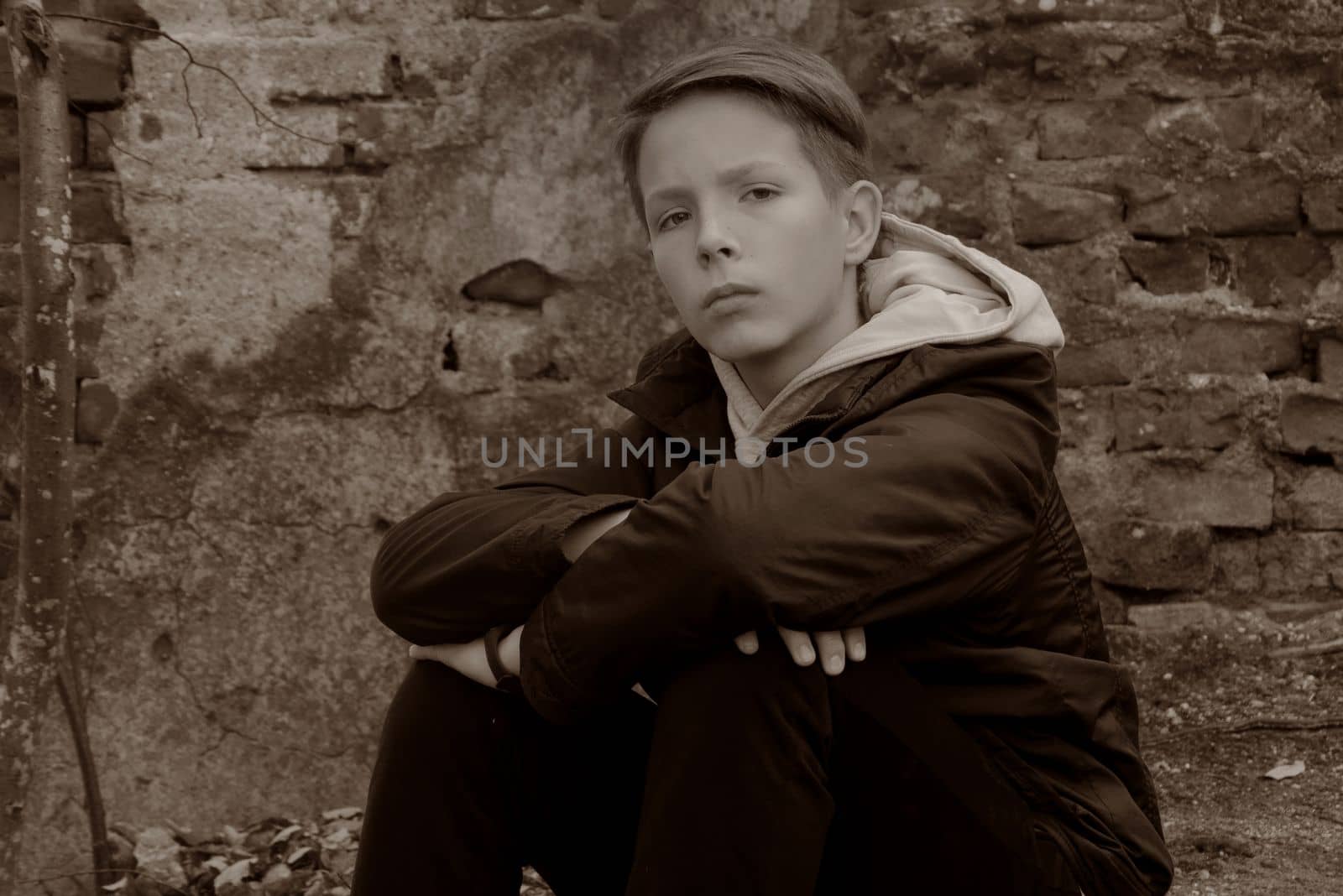 Beautiful boy 13-15 years old sits opposite a brick wall. Black and white portrait of a teenager against an old brick wall.