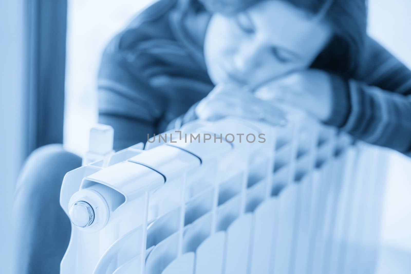 Woman wearing pullover sitting near heater radiator and hugs it by Mariakray