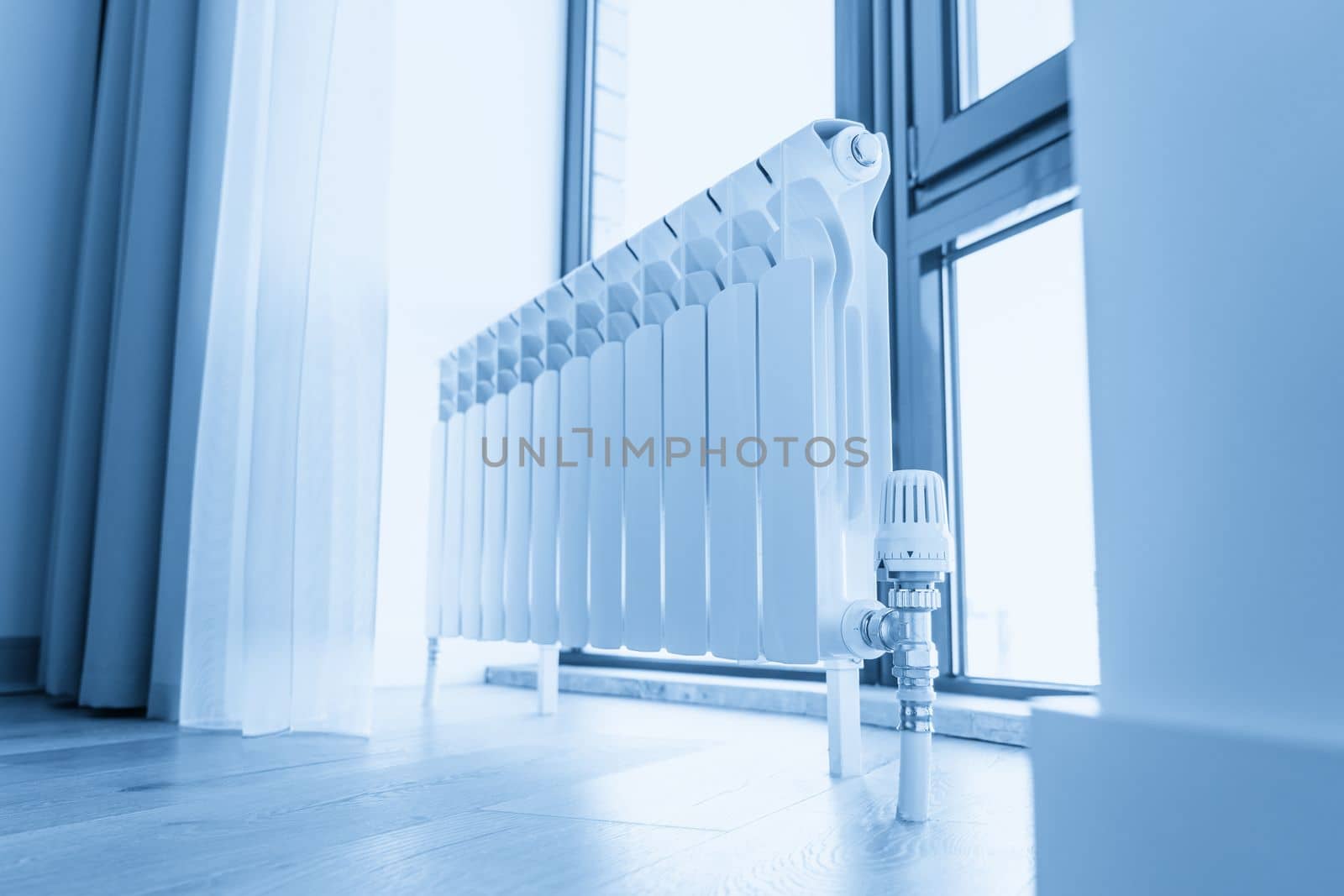 White big radiator with thermostat near window in modern room by Mariakray