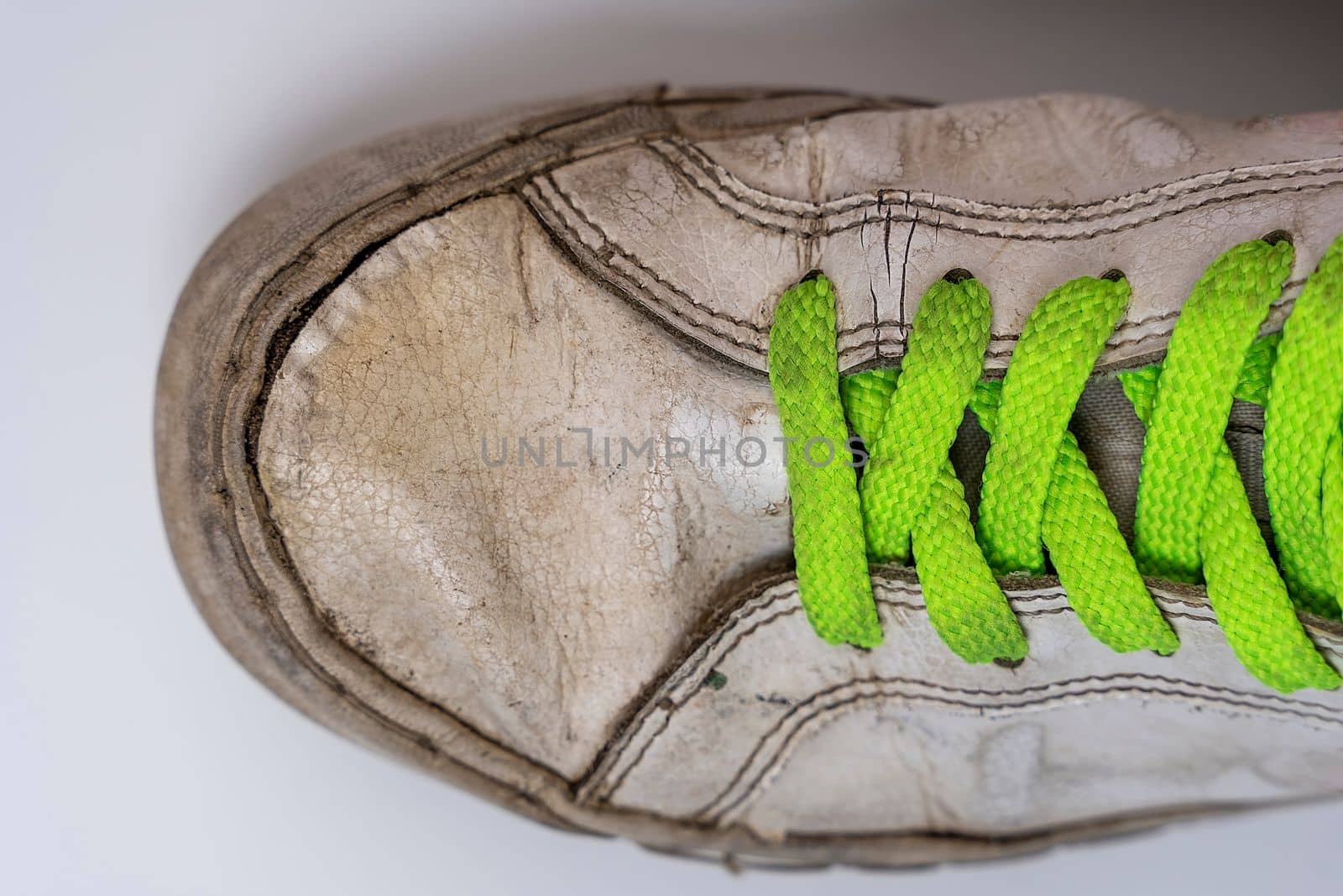 worn old torn white sneakers with colored laces on a white background. Close-up. Fashionable colored acid-colored shoelaces. top view