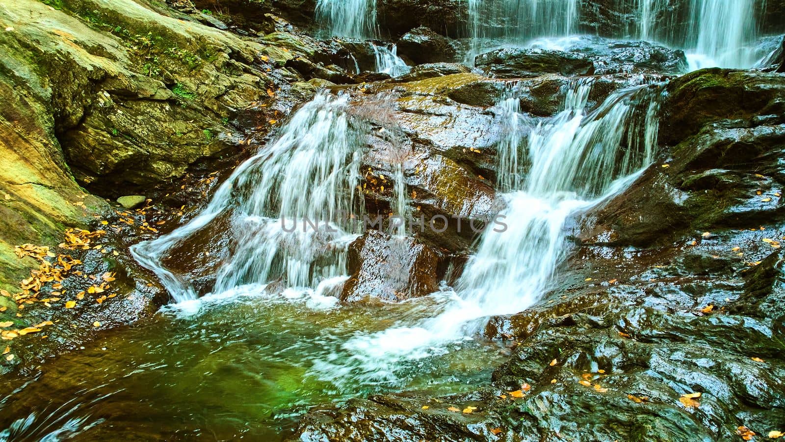 Image of Detail of lower waterfalls cascading softly over rocky surface with fall leaves
