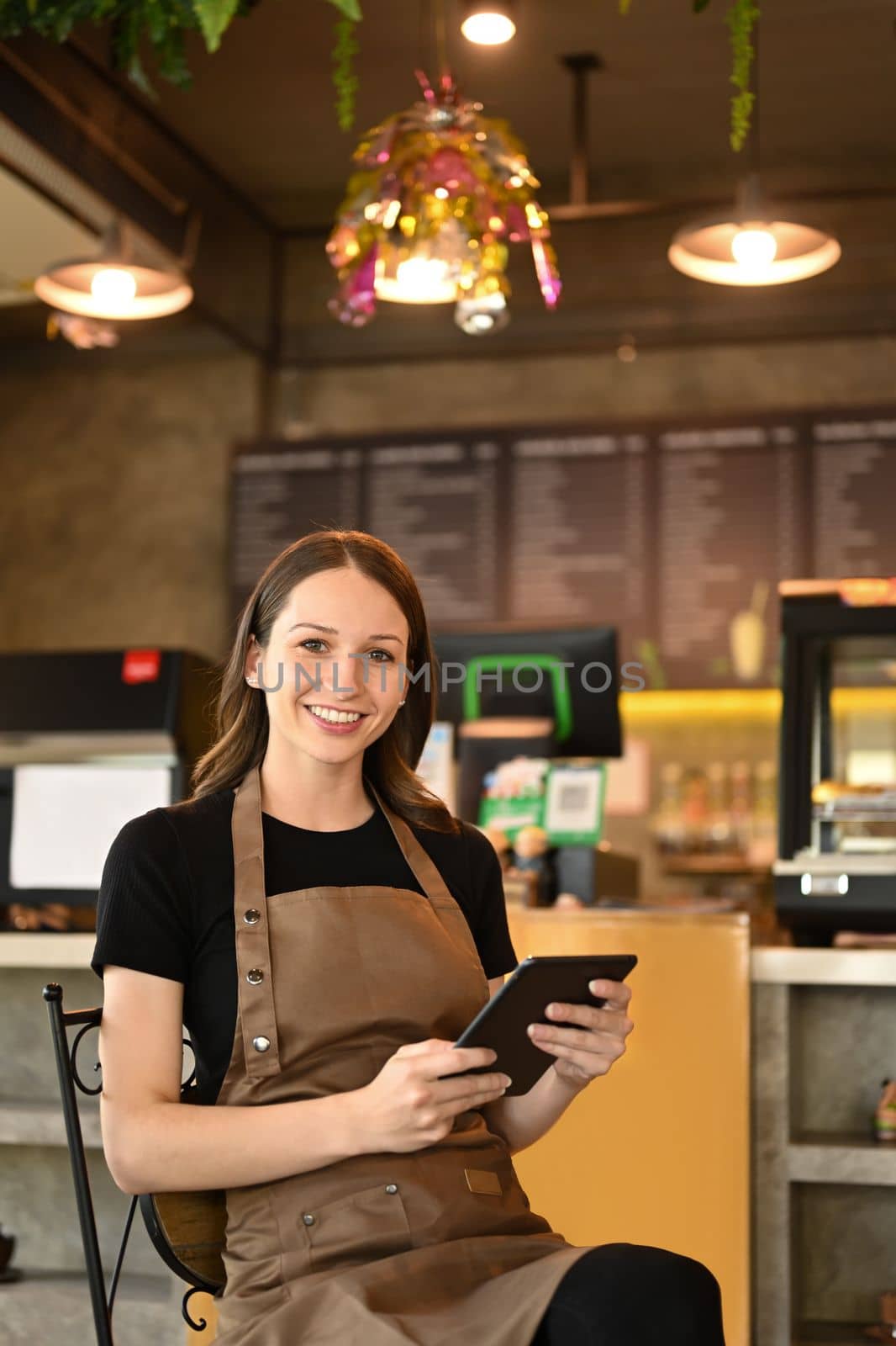 Image of successful small business owner using digital tablet and looking at camera while sitting in her modern coffee shop by prathanchorruangsak