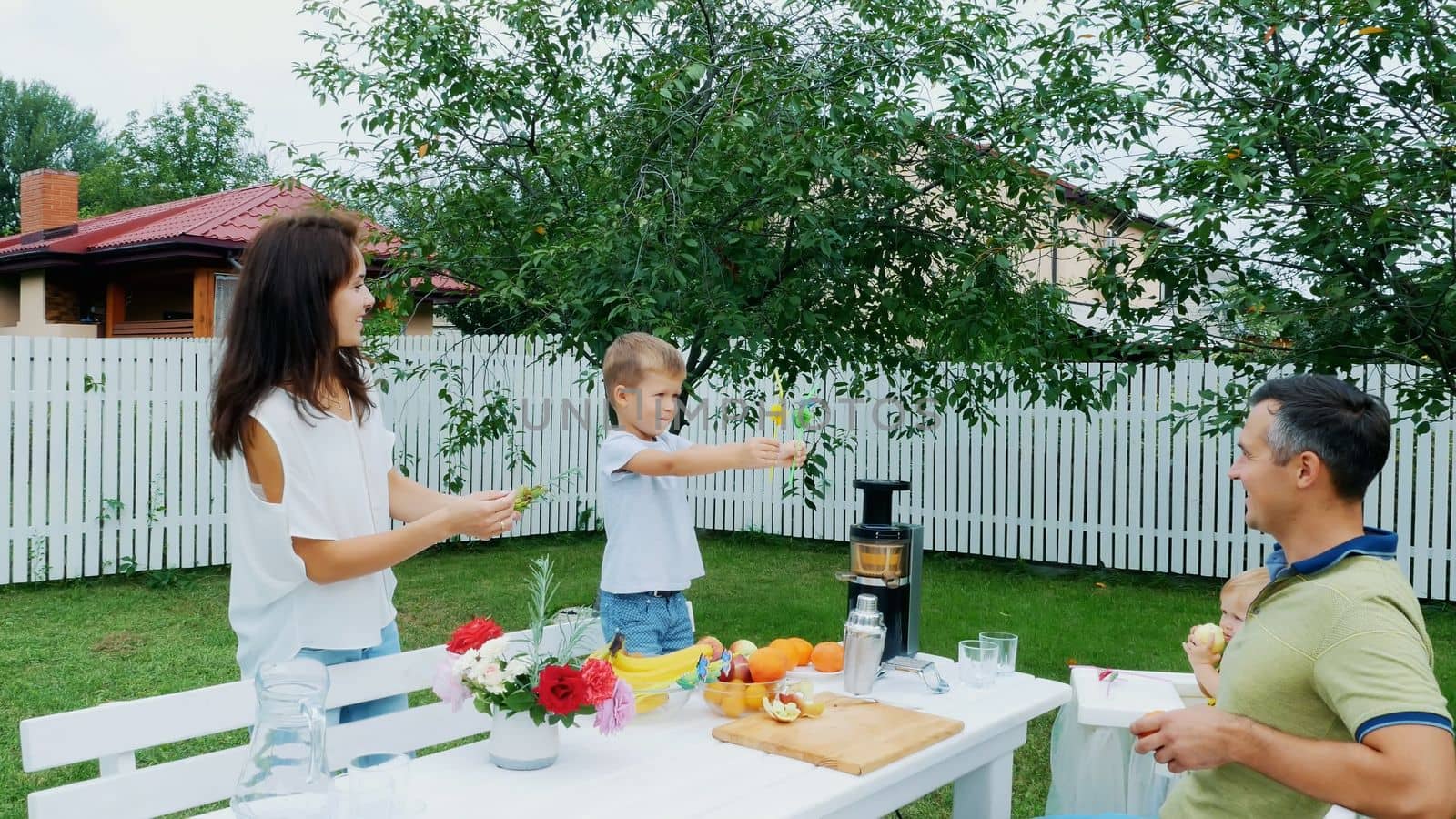summer, in the garden, four-year-old boy has decorated the straw for juice, boasts them before his father, mother and younger sister. The boy has fun, shows his tongue. High quality photo