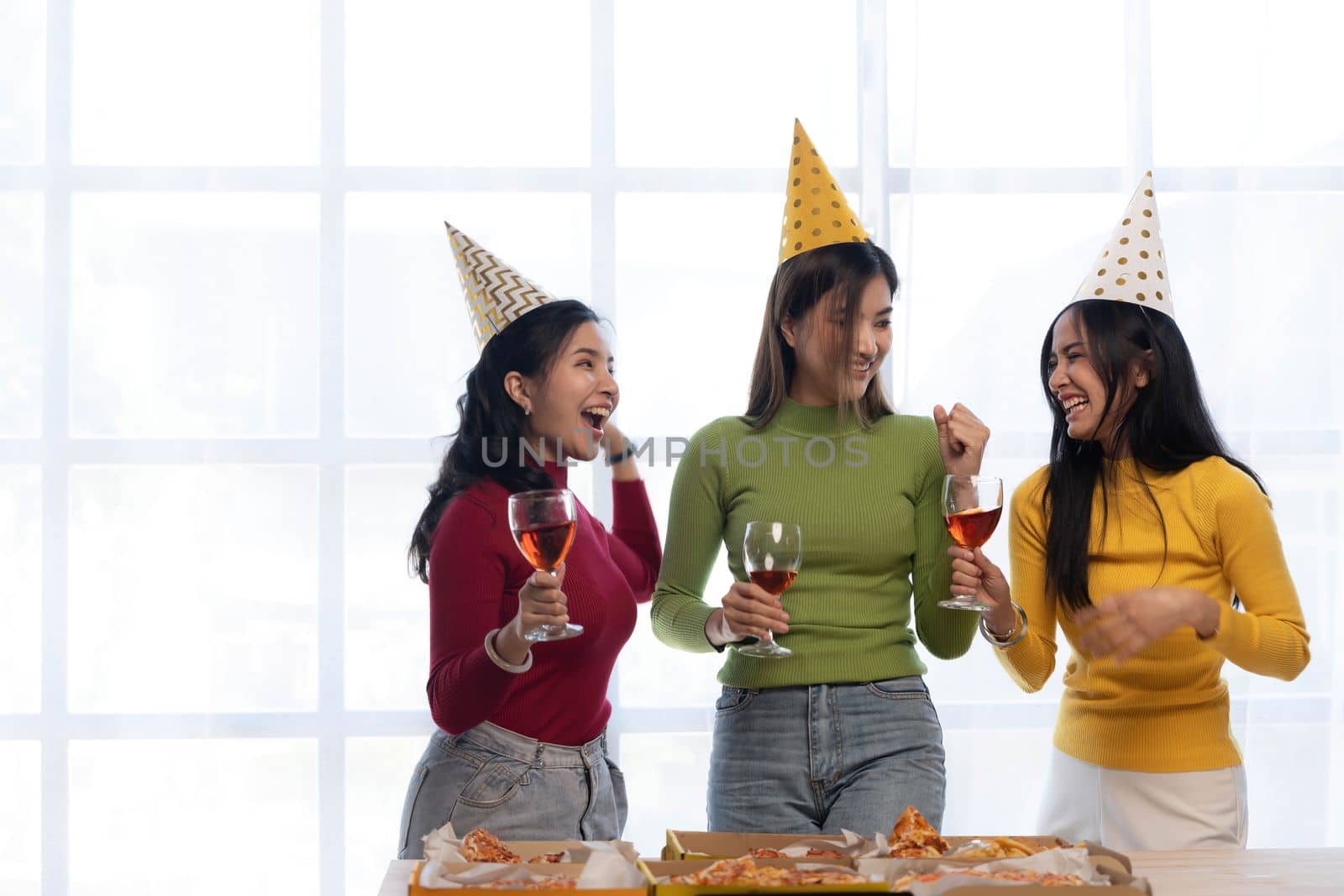 Group of happy young Asian people with friends celebrating clinking glasses during dinner party by wichayada