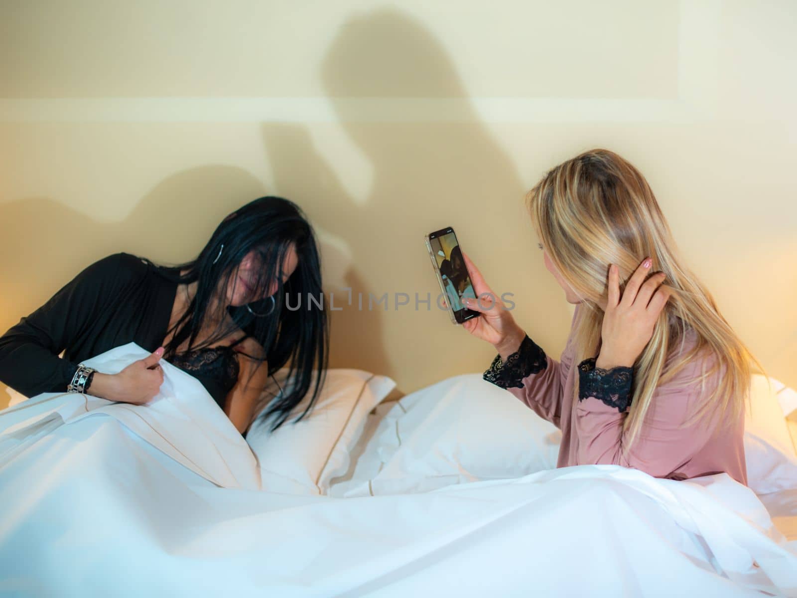 adorable diverse lgbt female couple in bodysuit lying in bed on cream sheets chating after sleeping by verbano