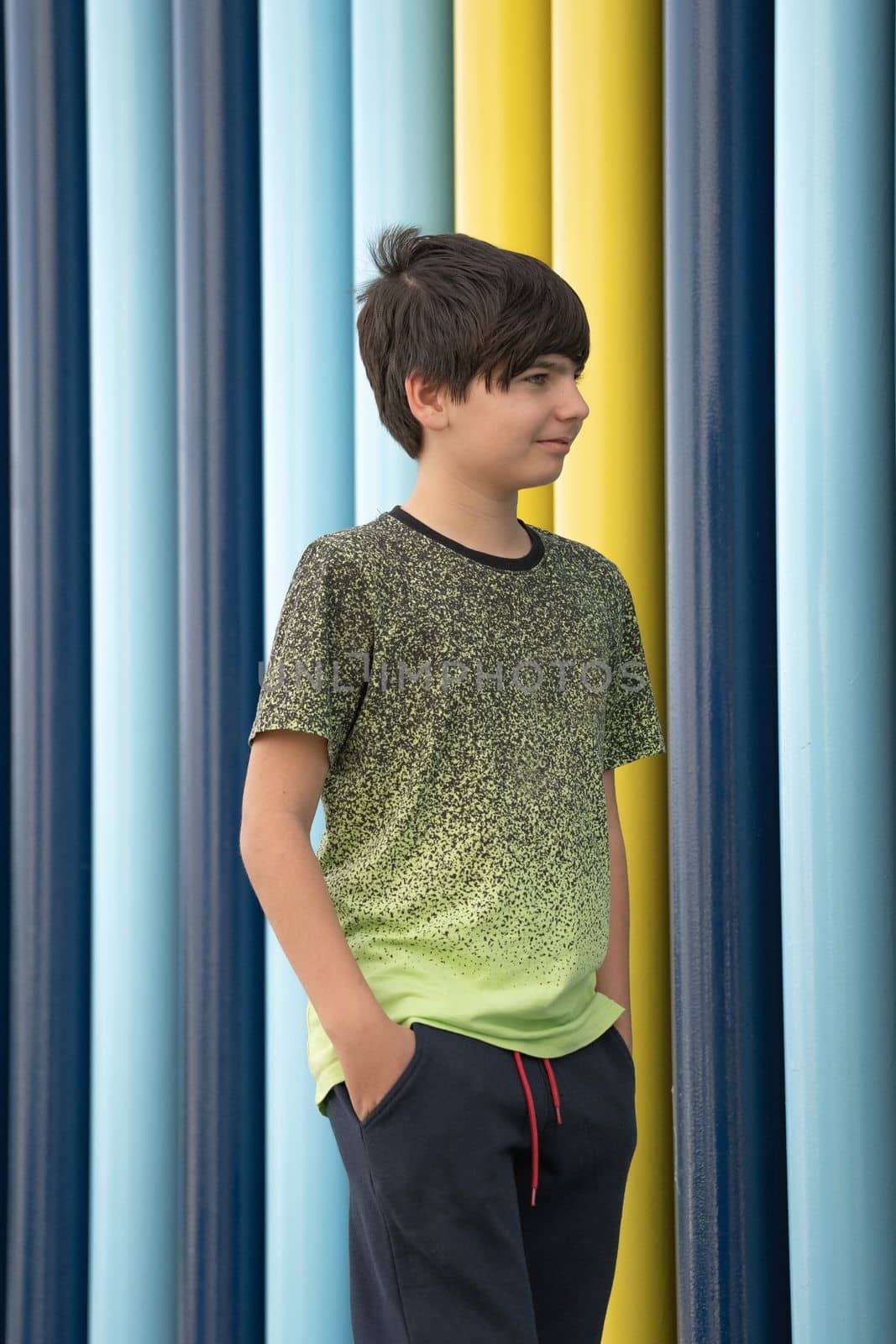 Caucasian boy wearing sport clothes standing with hands in pockets smiling and looking away on colourful background.