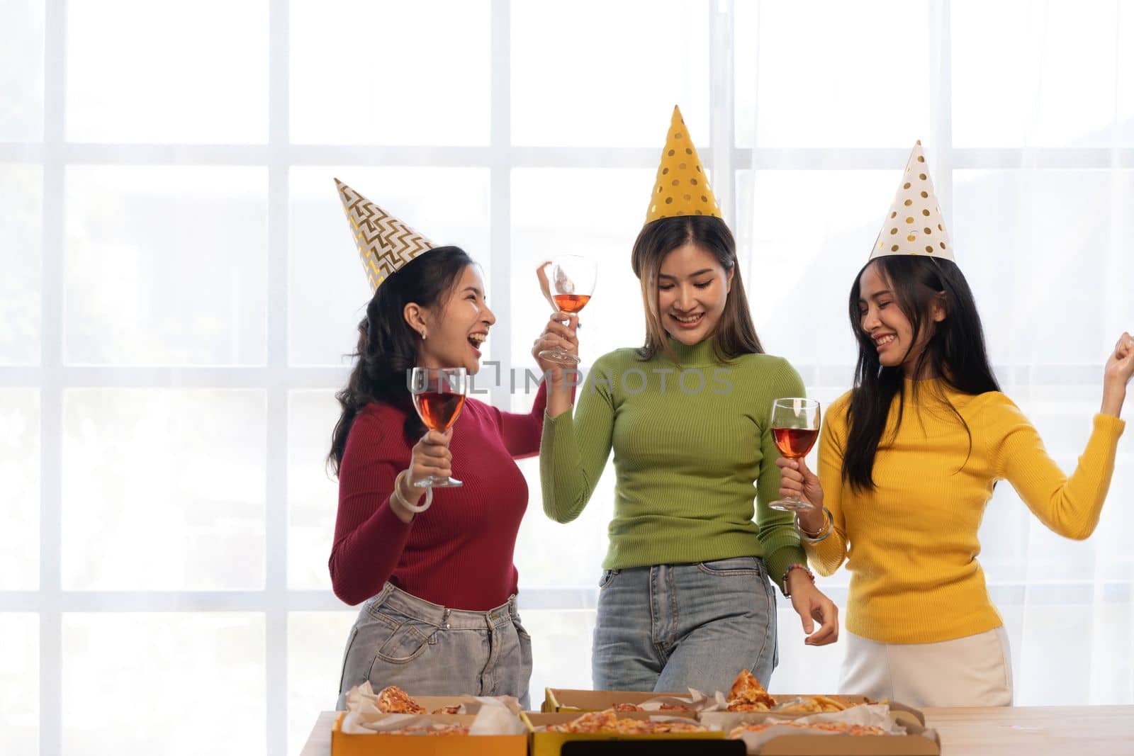 Group of happy young Asian people with friends celebrating clinking glasses during dinner party by wichayada