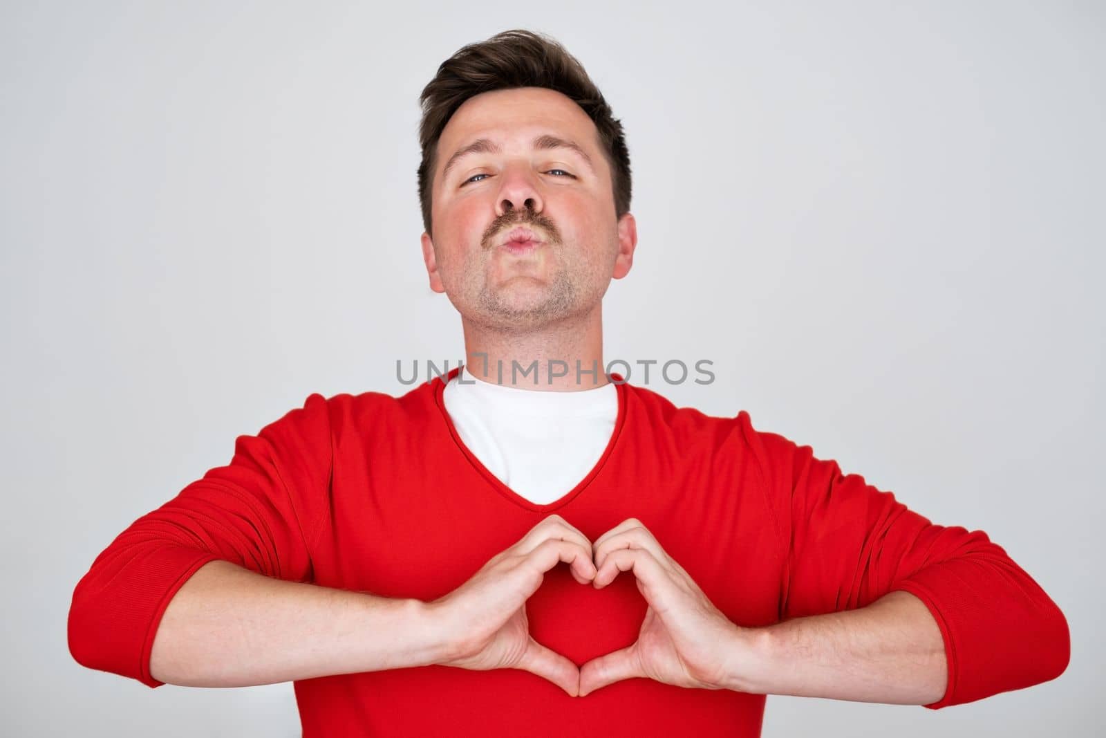 Young handsome man in love doing heart symbol shape with hands. Romantic concept. 