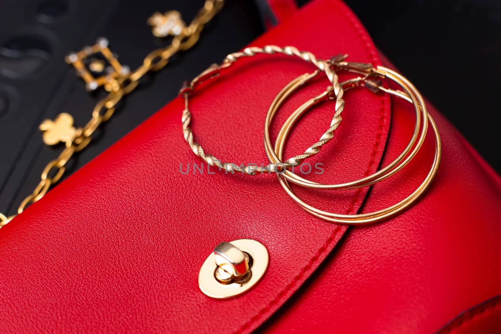 Gold ring earrings and costume jewelry lie on a little red leather bag. Close up