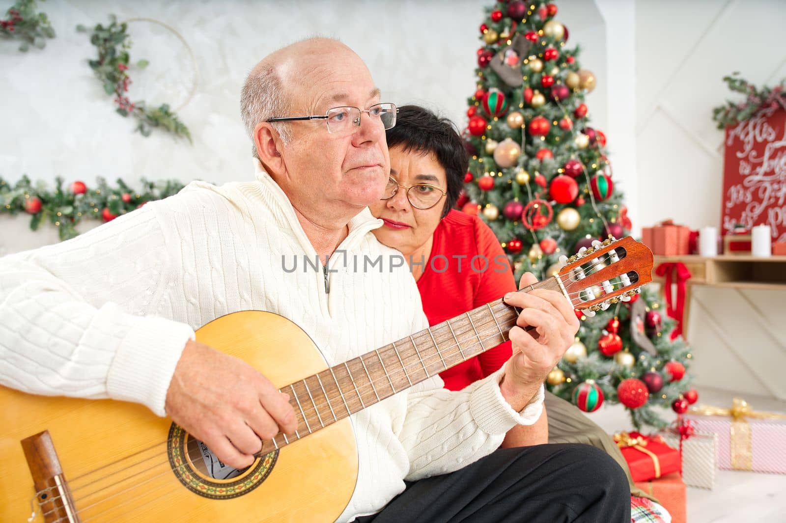 Father playing guitar during christmas. Happy man 60s playing guitar christmas songs. Happy christmas atmosphere.