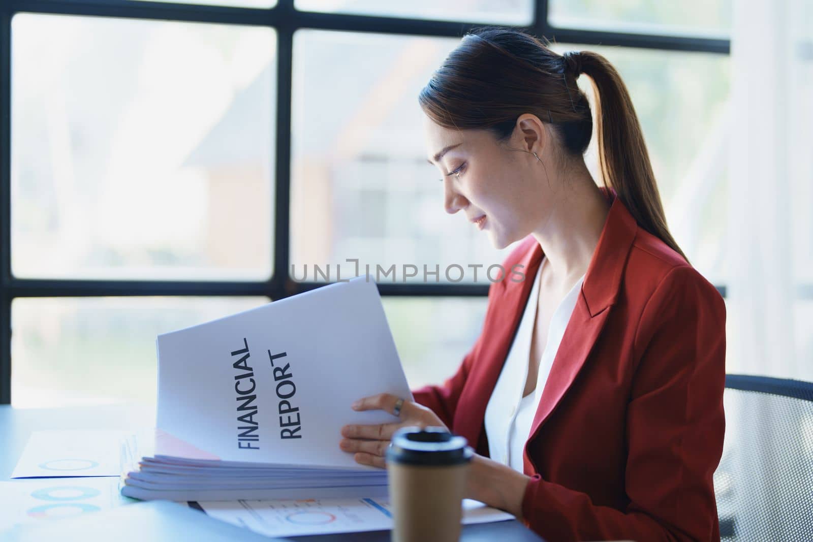 Portrait of a thoughtful Asian businesswoman looking at financial statements and making marketing plans using a computer on her desk by Manastrong