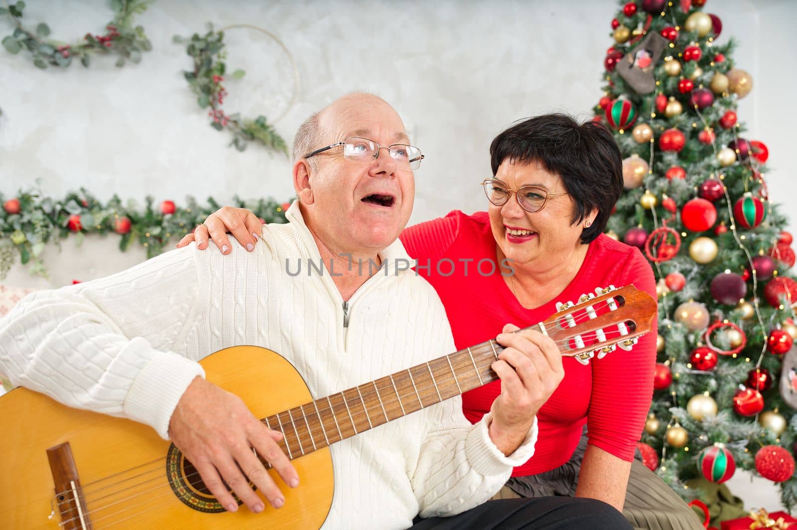 Father playing guitar during christmas. Happy man 60s playing guitar christmas songs. Happy christmas atmosphere.