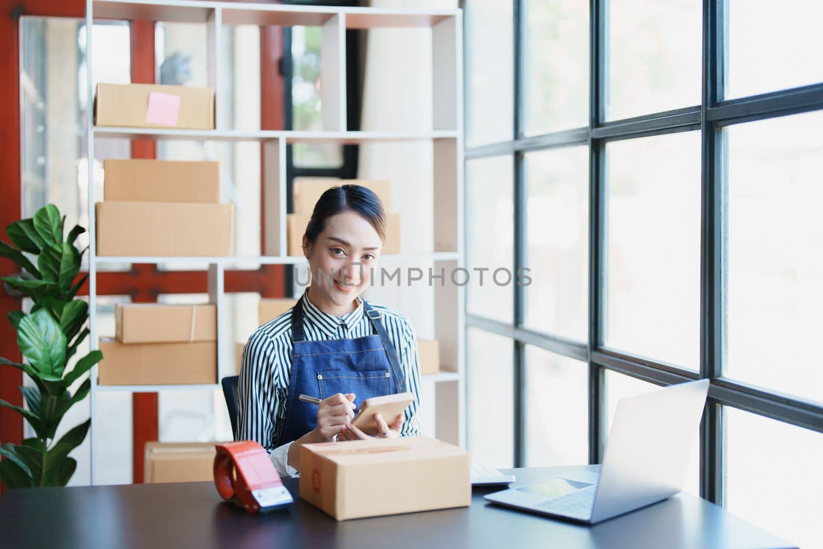 Starting small business entrepreneur of independent young Asian woman online seller is using computer and taking orders to pack products for delivery to customers. SME delivery concept by Manastrong