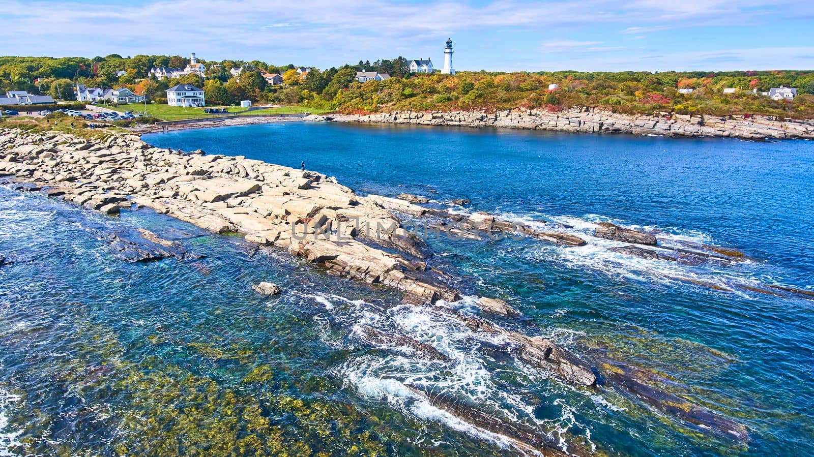 Image of Aerial over ocean and coast with shallow water in Maine and lighthouse with homes in background
