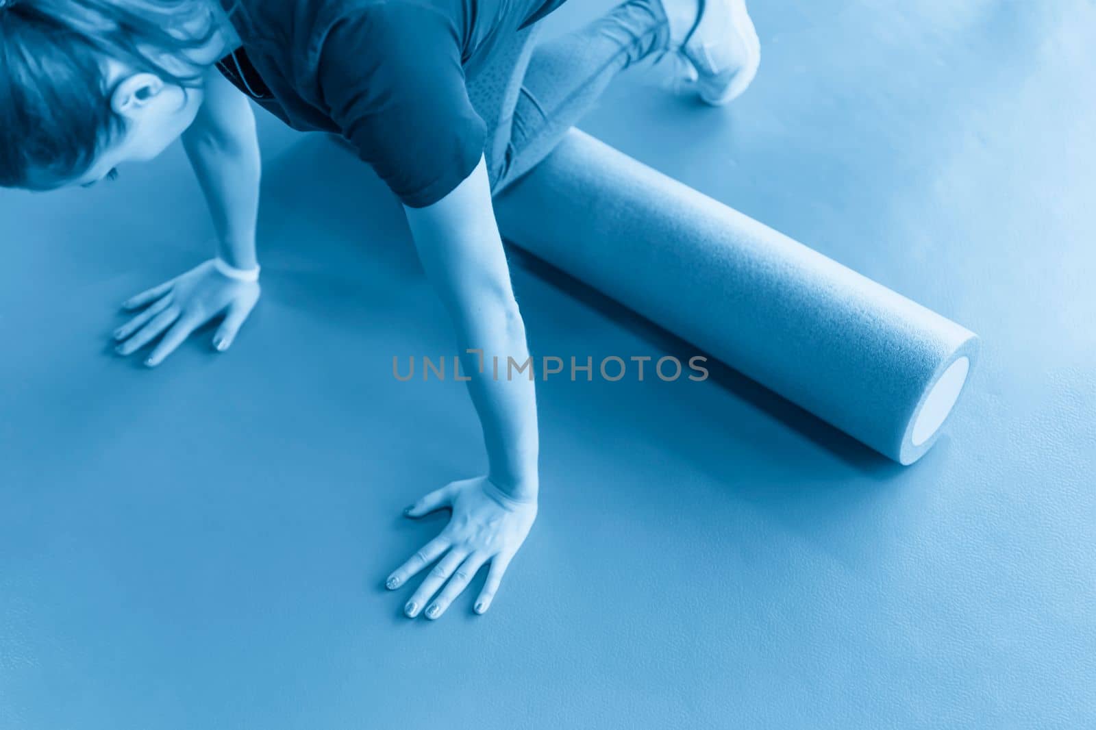 Attractive female doing foam roller exercise and posing in modern bright fitness center by Mariakray