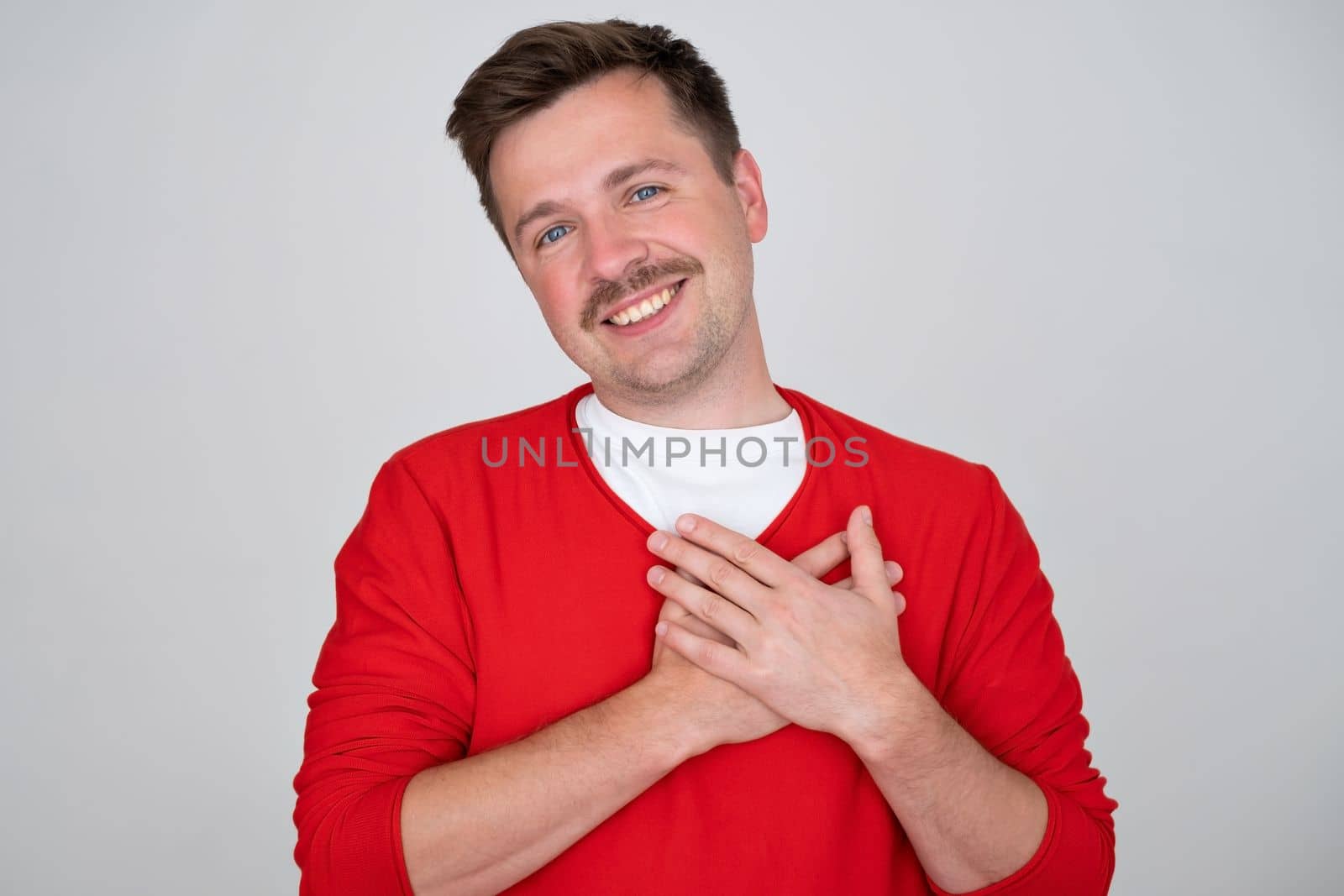  handsome male expresses his positive feeling to people who surround him, keeps hand on chest or heart