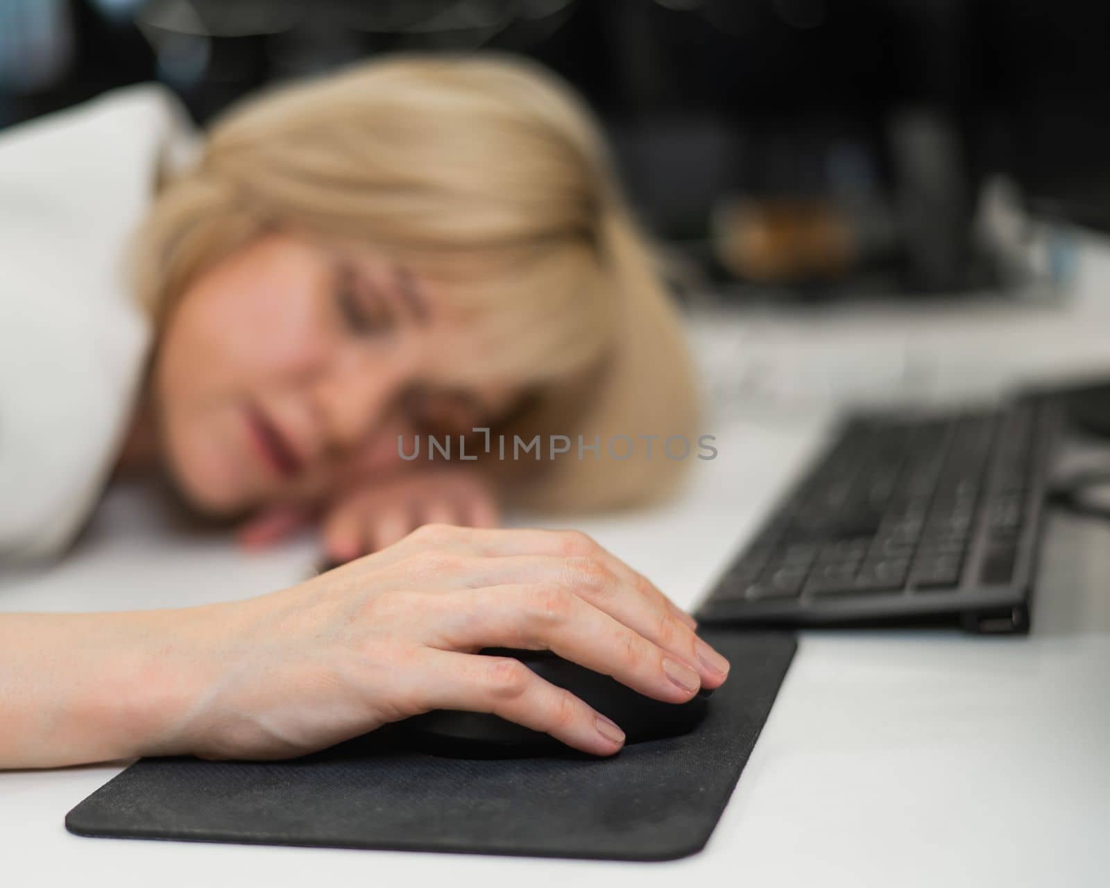 Caucasian blonde woman sleeping at her desk in the office. Blurred