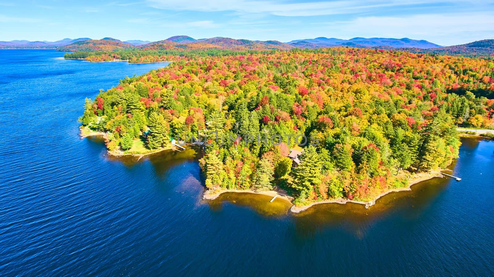 Blue water lake aerial focused on coastline filled with fall forests and mountains by njproductions