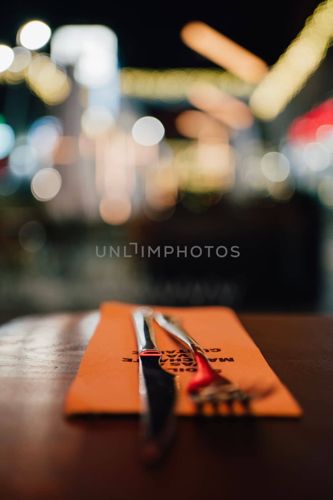 close up table setting in restaurant. Fork and a Knife and napkin.City night lights in background by papatonic